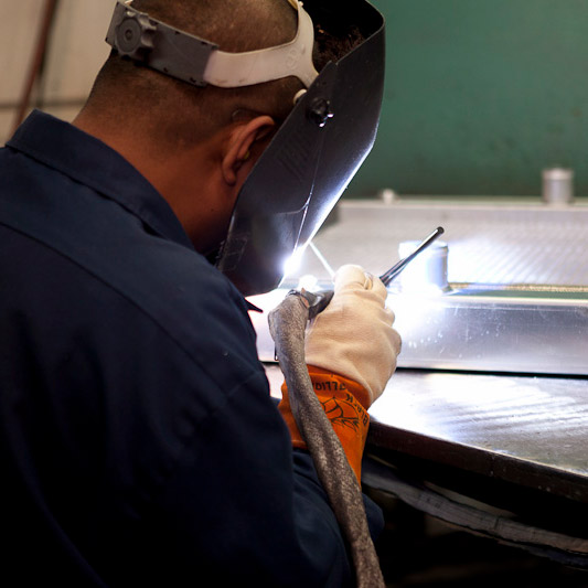 Best industrial cooling systems: A JB Radiator Specialties employee wearing a welding mask doing some precision work.