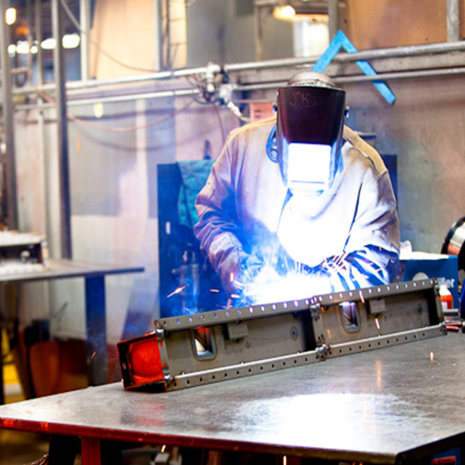 A JB Radiator Specialties employee wearing protective gear welding, sparks flying.